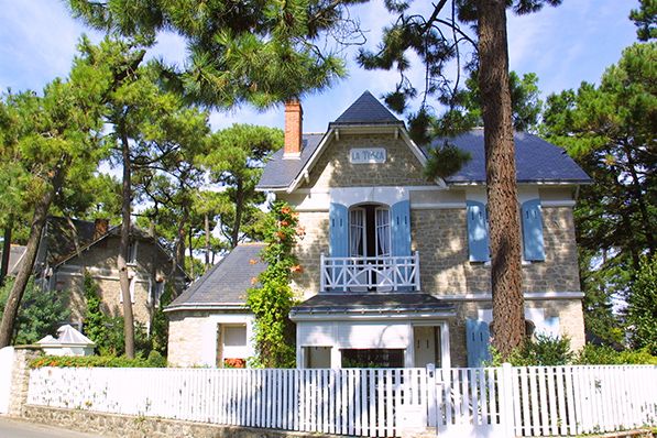 Photo d'une façade de villa bauloise typique à l'ombre des pins